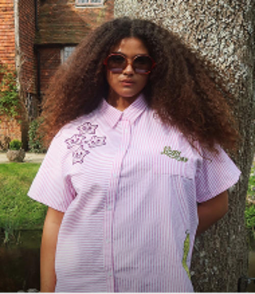 Woman wearing a Lazy Oaf pink striped shirt leaning against a tree.